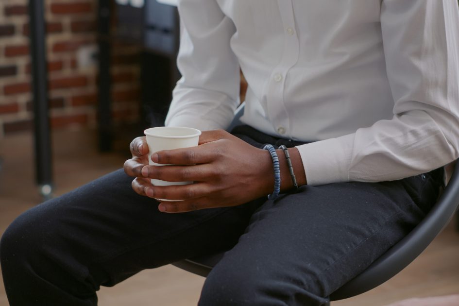 Close up of african american man fewling nervous while holding cup of coffee at aa meeting Close up of african american man fewling nervous while holding cup of coffee at aa meeting. Adult with anger management issues having hot drink in hands, attending therapy session.
